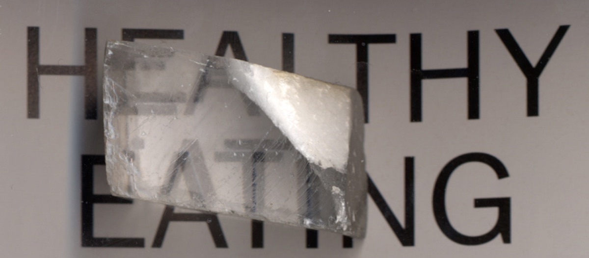A calcite crystal demonstrating birefringence: text viewed through it appears doubled because the crystal splits light into two rays - the same light-bending phenomenon that the MoOCl2 crystal pushes to a record level.